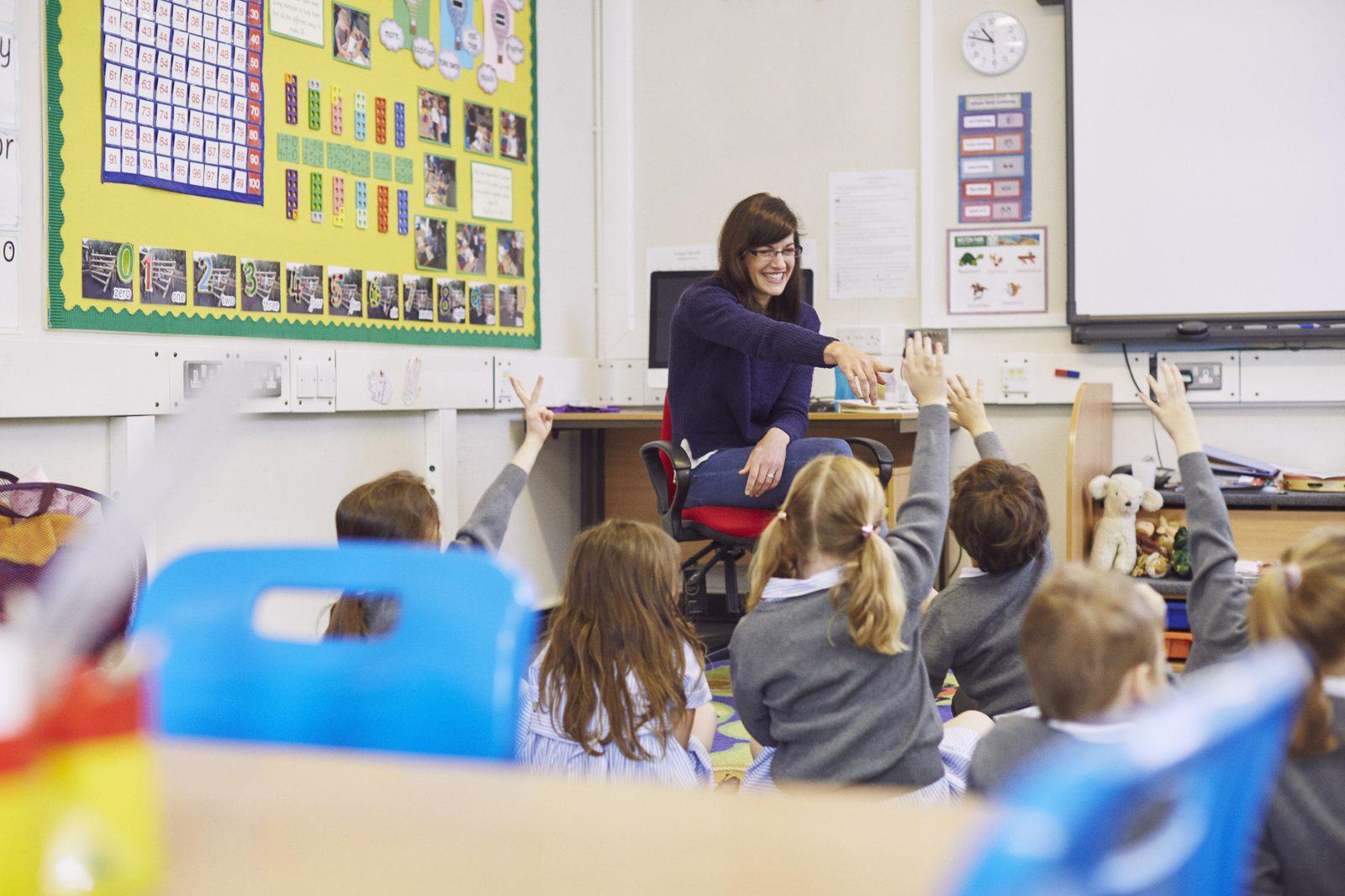 A full class of pupils with hands raised